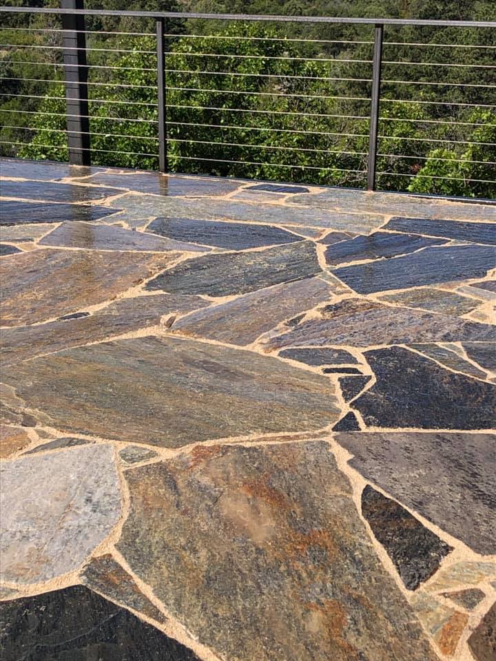 Photo of natural-stone looking pavers and cable railing on a rooftop deck amidst the trees.