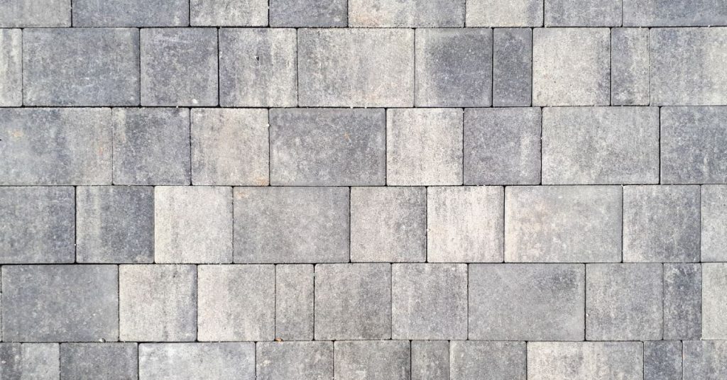 A series of gray paving stones, making up the surface of a home balcony, layed over interlocking stone deck pavers.